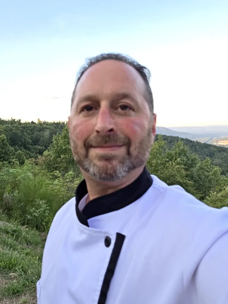 Chef Joe in his chef coat with a mountain view behind him