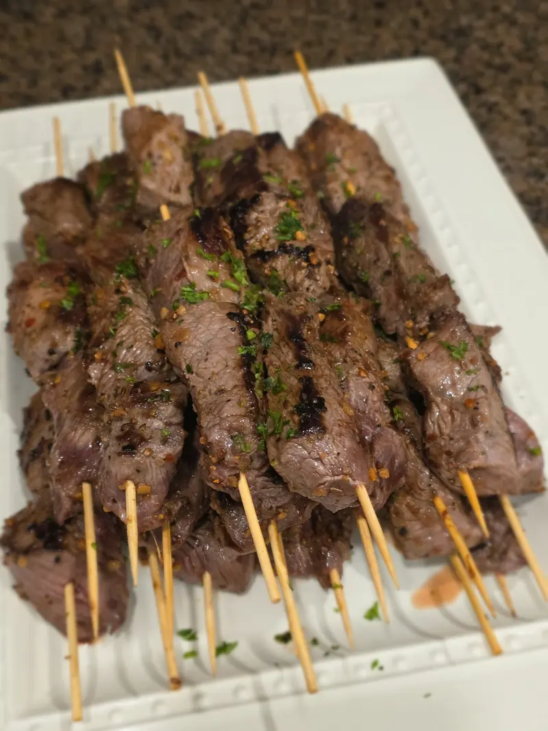 Grilled steak skewers on a white platter